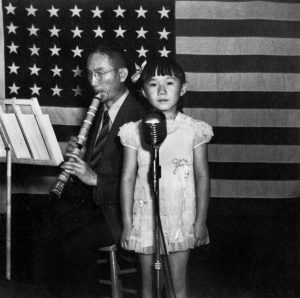A young Asian child standing in front of the U.S. flag