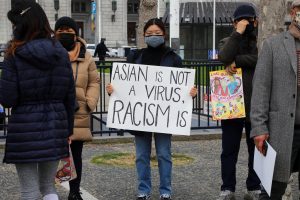 A person holding a sign that reads "Asian is not a virus, racism is"