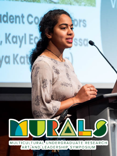 Person standing at a podium deliver a presentation with the MURALS Multicultural Undergraduate Research Art and Leadership Symposium wordmark